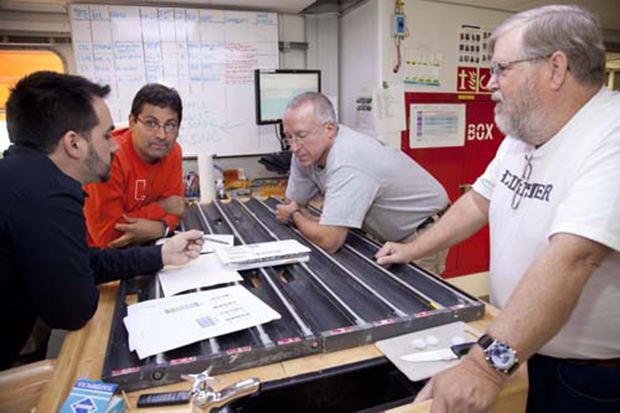 four men talk around a table covered with core samples
