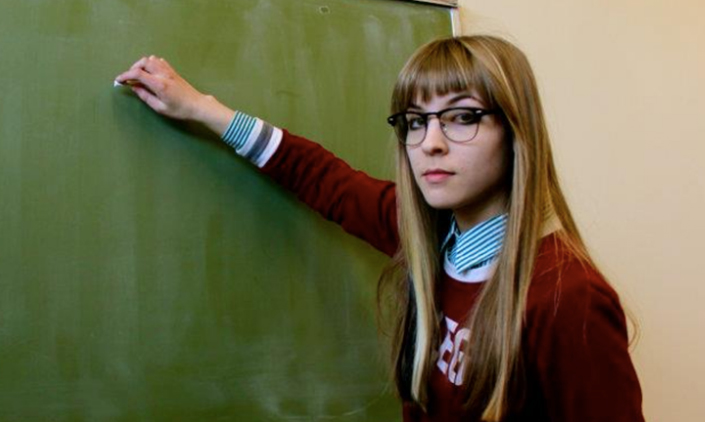 young woman in glasses prepares to write on blackboard