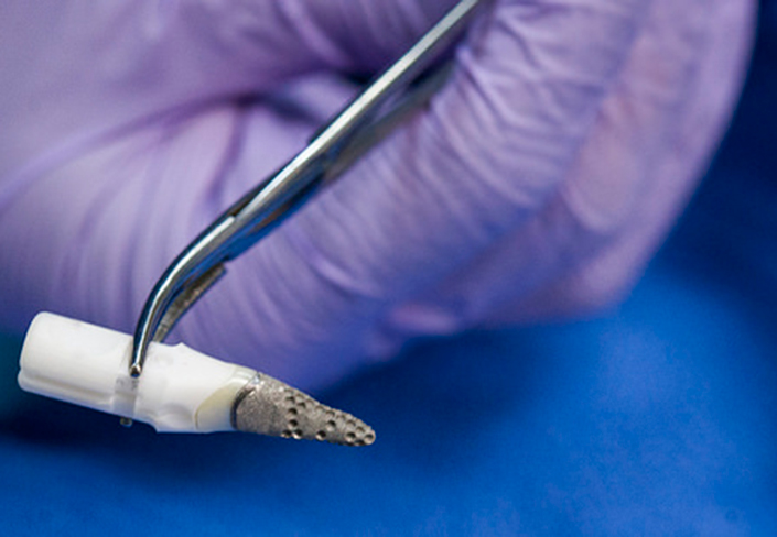 hand using a surgical tool to hold an artificial tooth