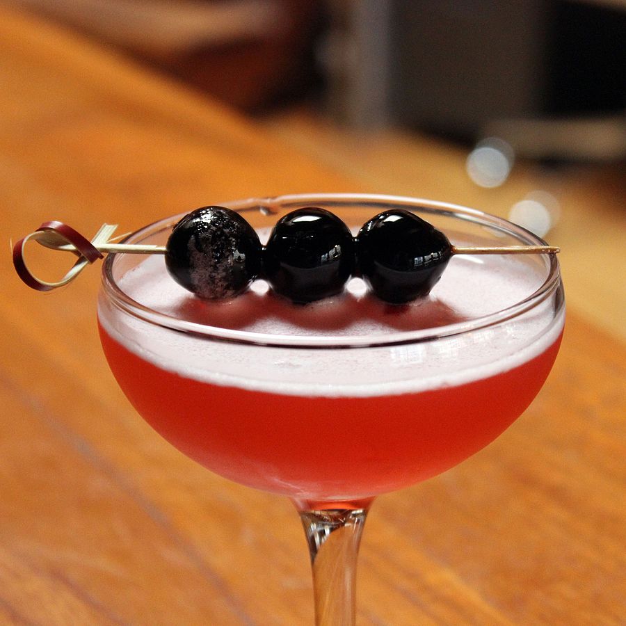 a cocktail glass filled with liquor and garnished with cherries