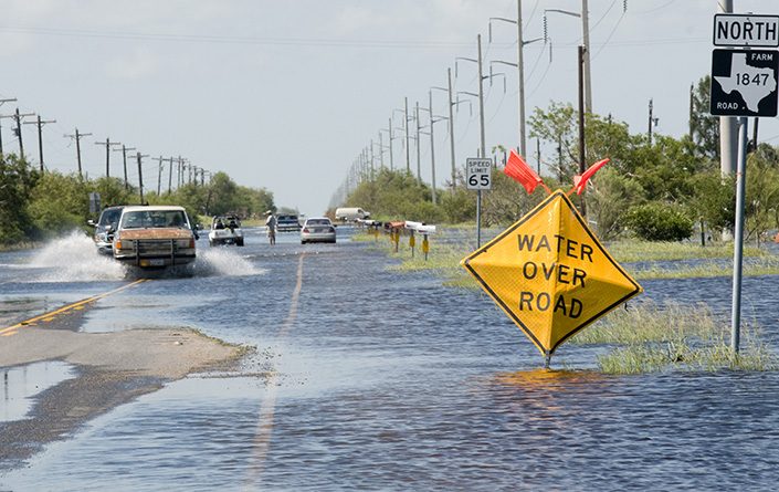 Cars attempt to cross a flooded roadway.