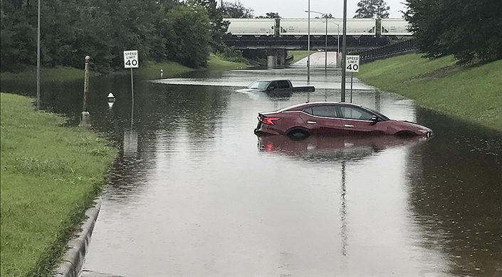 An abandoned car in a flooded street near an overpass